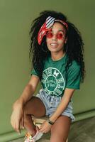 attractive black african american woman posing in stylish hipster outfit on green background photo