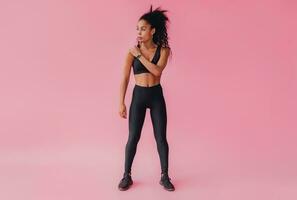 attractive black african american woman in black leggins fitness outfit on pink background photo