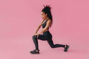 attractive black african american woman in black leggins fitness outfit on pink background photo