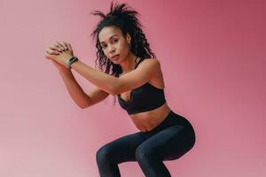 attractive black african american woman in black leggins fitness outfit on pink background photo