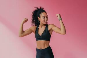 attractive black african american woman in black leggins fitness outfit on pink background photo