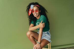 attractive black african american woman posing in stylish hipster outfit on green background photo