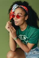 attractive black african american woman posing in stylish hipster outfit on green background photo