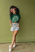 attractive black african american woman posing in stylish hipster outfit on green background photo