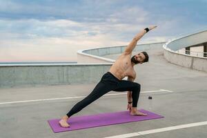 atractivo hansome hombre con atlético fuerte cuerpo haciendo Mañana yoga asana al aire libre foto