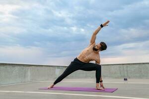 atractivo hansome hombre con atlético fuerte cuerpo haciendo Mañana yoga asana al aire libre foto