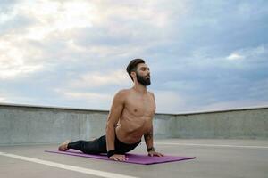 attractive hansome man with athletic strong body doing morning yoga asana outdoors photo