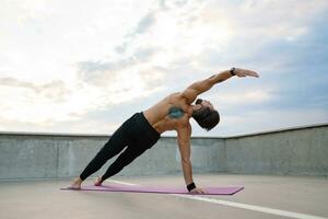 atractivo hansome hombre con atlético fuerte cuerpo haciendo Mañana yoga asana al aire libre foto