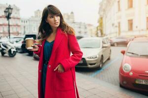 elegante mujer en rojo Saco caminando en calle con café foto