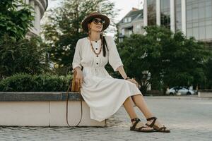 beautiful woman walking in street on vacation dressed in white summer fashion dress photo