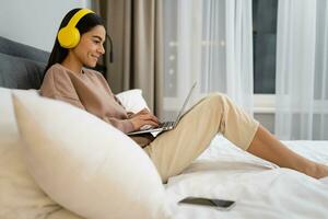 young woman at home in casual outfit working remote job on laptop sitting on bed photo