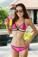 pretty slim woman playing with watergun toy at pool on summer tropical vacation photo