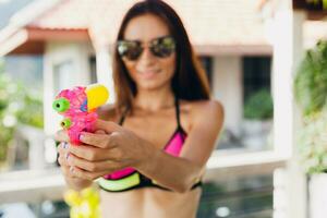 bonito Delgado mujer jugando con pistola de agua juguete a piscina en verano tropical vacaciones foto