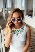 attractive woman in white dress in summer cafe in sunglasses talking on phone photo