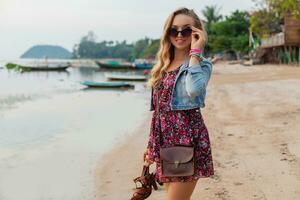 stylish woman in summer dress vacation walking on beach with shoes in hand photo