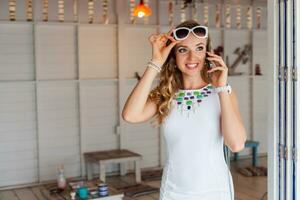 attractive woman in white dress in summer cafe in sunglasses talking on phone photo