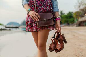 elegante mujer en verano vestir vacaciones caminando en playa con Zapatos en mano foto