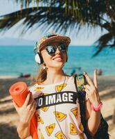 joven hermosa mujer caminando en playa con yoga estera foto