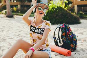 attractive hipster woman sitting on beach listening to music on headphones photo