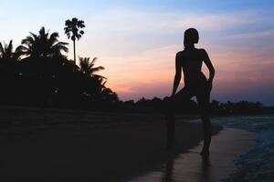 joven hermosa Delgado mujer en pie en playa a amanecer, tropical vacaciones foto