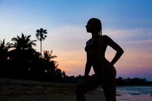 joven hermosa Delgado mujer en pie en playa a amanecer foto