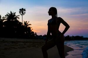 joven hermosa Delgado mujer en pie en playa a amanecer foto
