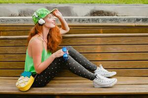 young stylish hipster ginger woman, sitting on bench, listening music photo