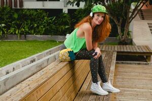 young stylish hipster ginger woman, sitting on bench, listening music photo