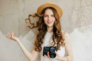 young pretty smiling happy woman in straw hat holding vintage photo camera, long curly hair