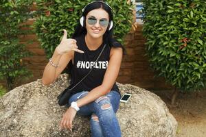 young stylish hipster woman in black t-shirt, jeans, listening to music on headphones photo