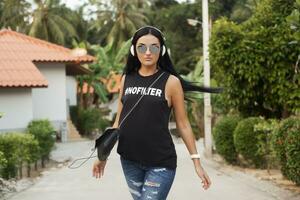 joven elegante hipster mujer en negro camiseta, vaqueros, escuchando a música en auriculares foto