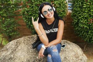 joven elegante hipster mujer en negro camiseta, vaqueros, escuchando a música en auriculares foto