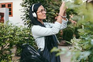 young stylish woman walking with smartphone, listening to music on headphones photo