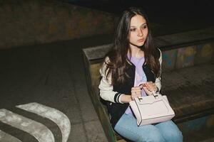 young stylish hipster woman, swag outfit, jeans, cool accessories, sitting on ground with purse photo