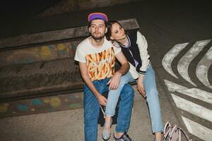 cool young stylish hipster couple in love, swag outfit, jeans, embrace, cool accessories, sitting happy, having fun photo