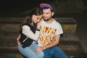 young stylish hipster couple in love, swag outfit, jeans, embrace, cool accessories, sitting happy, having fun photo