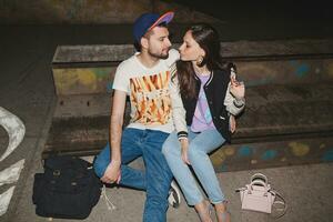 young stylish hipster couple in love, swag outfit, jeans, embrace, cool accessories, sitting happy, having fun photo