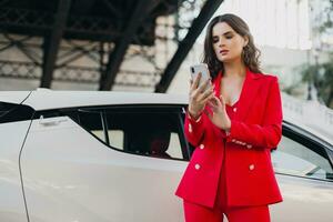 hermosa sexy mujer en rojo traje posando a coche hablando en negocio en teléfono foto