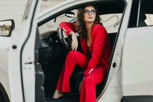 beautiful sexy rich business woman in red suit sitting in white car, wearing glasses photo