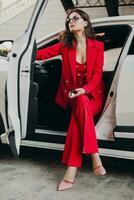 beautiful sexy rich business woman in red suit sitting in white car, wearing glasses photo