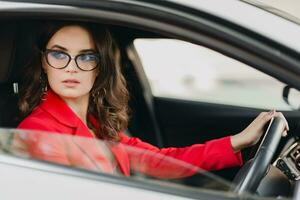 beautiful sexy rich business woman in red suit sitting in white car, wearing glasses photo