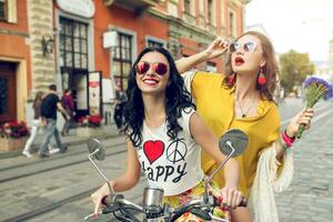 two young beautiful hipster women riding on motorbike city street photo