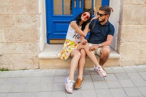 young beautiful hipster couple in love sitting on old city street photo
