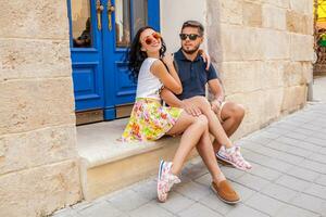 young beautiful hipster couple in love sitting on old city street photo