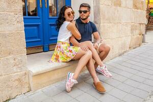 young beautiful hipster couple in love sitting on old city street photo