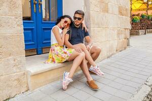 young beautiful hipster couple in love sitting on old city street photo