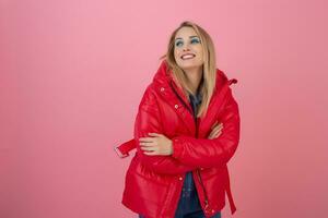 blond happy attractive active woman posing on pink background in colorful winter down jacket of red color, having fun, warm coat fashion trend, smiling photo