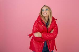 blond happy attractive active woman posing on pink background in colorful winter down jacket of red color, having fun, warm coat fashion trend, smiling photo