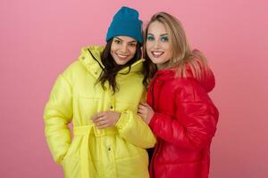 two attractive girl friends active women posing on pink background in colorful winter down jacket of bright red and yellow color having fun together, warm coat fashion trend, sincerely laughing photo