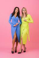 two stylish sexy attractive women posing full height on pink background in stylish colorful dresses of blue and yellow color, summer fashion trend photo